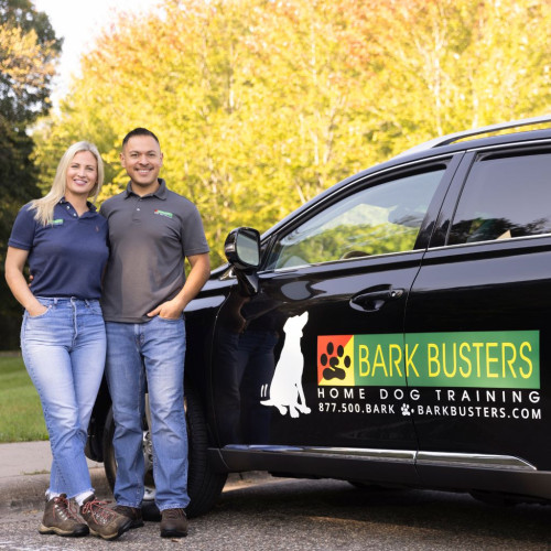 Dog training couple standing next a Bark Busters branded vehicle