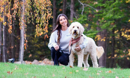 Woman kneeling with her dog in a park with autumn trees