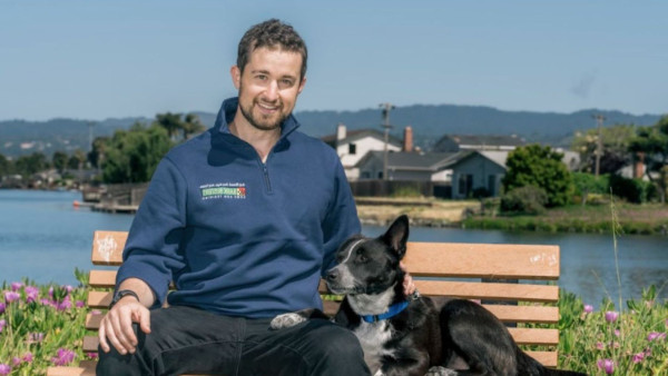 Dog trainer resting on a bench with a small white dog