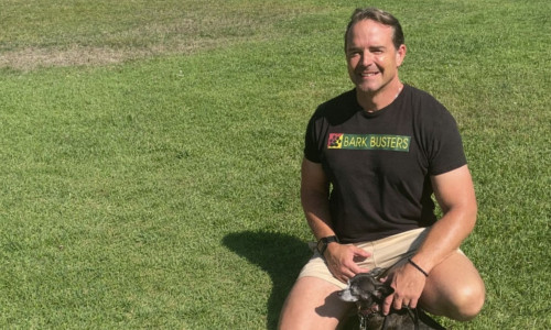 Man with a small dog sitting in a grassy field